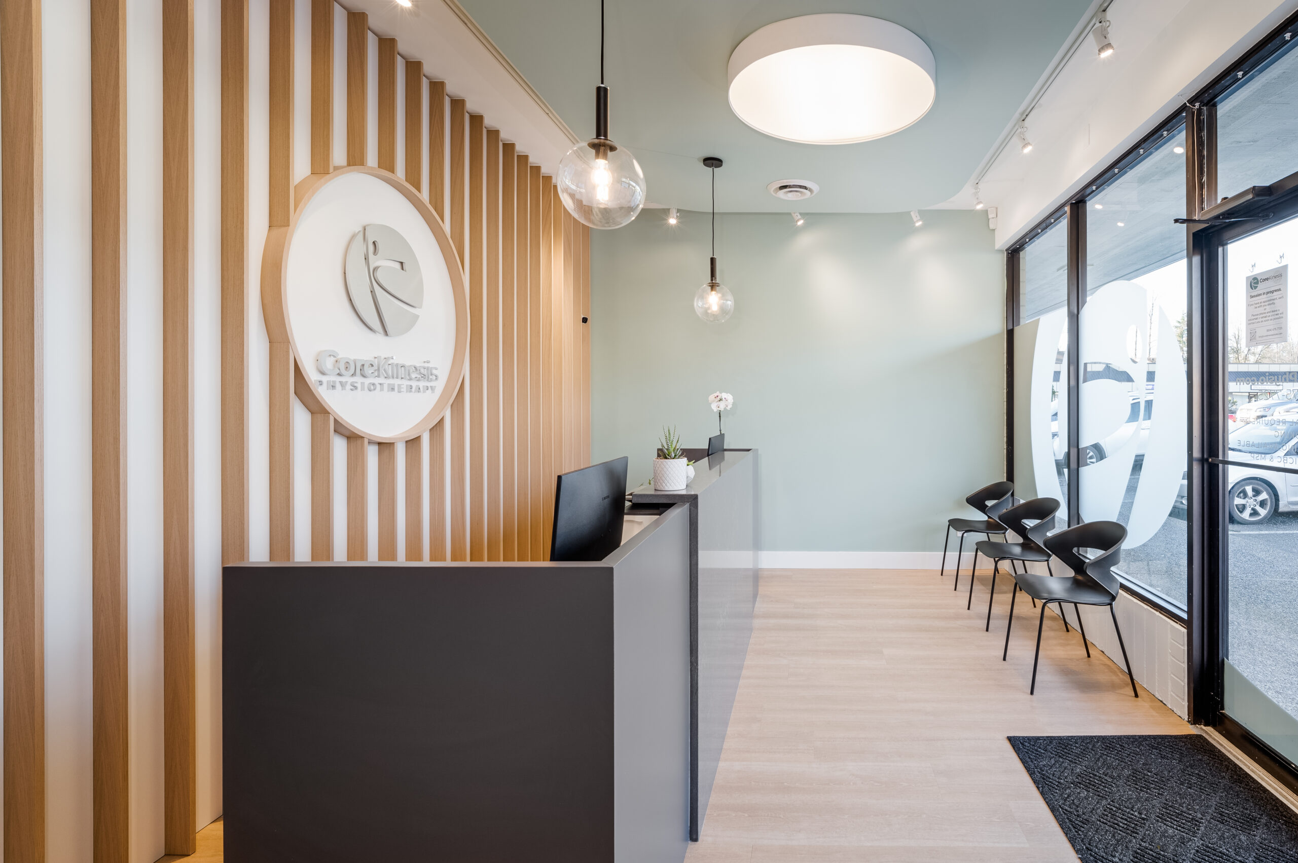 Reception at Core Kinesis Physiotherapy. Has seating for patients with wooden slats and logo on back feature wall